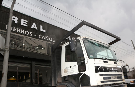 Fachada del local Real Home en Pilar con camión cargado de materiales saliendo para entrega